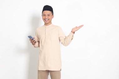 Koko tişörtlü yakışıklı Asyalı Müslüman adamın portresi. Kafasında cep telefonu olan, malı parmağıyla gösteren ve gösteren. Sosyal medya konsepti. Beyaz arkaplanda izole edilmiş resim