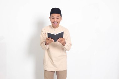 Koko gömlekli çekici Asyalı Müslüman adamın portresi. Peci kitabı okuyor. Beyaz arkaplanda izole edilmiş resim