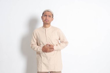 Koko tişörtlü dindar Asyalı Müslüman adamın portresi midesinde acı hisseden, açlığa dayanan. Karnım ağrıyor ve yemek konseptine açım. Beyaz arkaplanda izole edilmiş resim