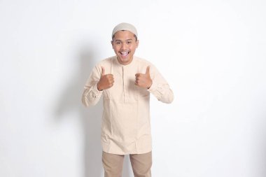 Koko gömlekli çekici Asyalı Müslüman adamın portresi baş parmağını gösteriyor, iyi iş el hareketi. Onaylama konsepti. Beyaz arkaplanda izole edilmiş resim