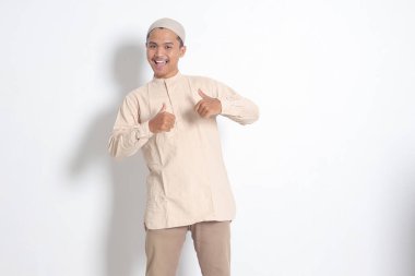 Koko gömlekli çekici Asyalı Müslüman adamın portresi baş parmağını gösteriyor, iyi iş el hareketi. Onaylama konsepti. Beyaz arkaplanda izole edilmiş resim