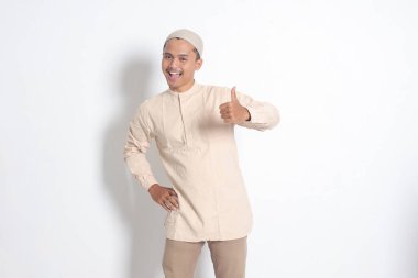Koko gömlekli çekici Asyalı Müslüman adamın portresi baş parmağını gösteriyor, iyi iş el hareketi. Onaylama konsepti. Beyaz arkaplanda izole edilmiş resim