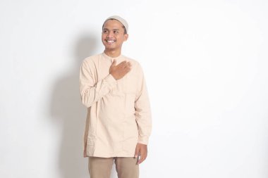 Koko tişörtlü çekici Asyalı Müslüman adamın portresi. Kafatası şapkalı ve birini içeri davet ediyor. Beyaz arkaplanda izole edilmiş resim