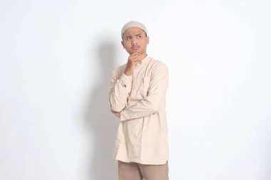 Kafası karışmış Koko tişörtlü Asyalı Müslüman adamın portresi. Kafasında kafatası olan ve eli çenesinde soru soran bir adam. Eğitim konsepti. Beyaz arkaplanda izole edilmiş resim