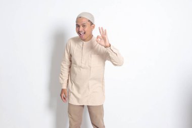 Koko tişörtlü yakışıklı Asyalı müslüman adamın portresi. Kafasında kafatası var. El hareketi yapıyor ve kameraya gülümsüyor. Onaylama konsepti. Beyaz arkaplanda izole edilmiş resim