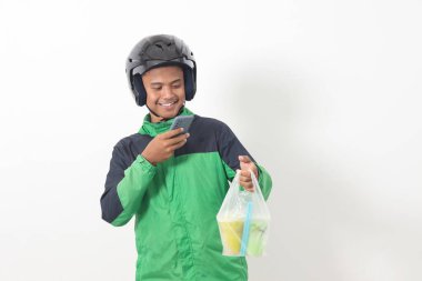 Portrait of Asian online taxi driver wearing green jacket and helmet delivering the beverages in plastic cup to customer, while using mobile phone. Isolated image on white background clipart