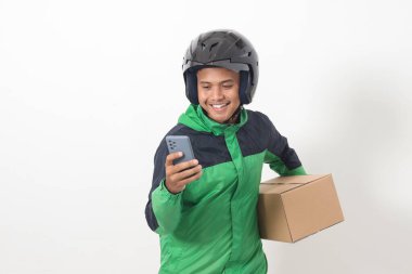 Yeşil ceket ve kask giyen Asyalı kurye sürücüsü portresi. Müşteri için paket ve kutu taşırken cep telefonu kullanıyor ve sipariş alıyor. Beyaz arkaplanda izole edilmiş resim