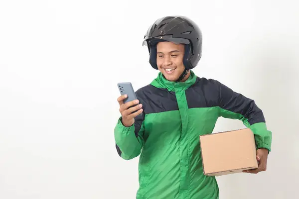 Yeşil ceket ve kask giyen Asyalı kurye sürücüsü portresi. Müşteri için paket ve kutu taşırken cep telefonu kullanıyor ve sipariş alıyor. Beyaz arkaplanda izole edilmiş resim