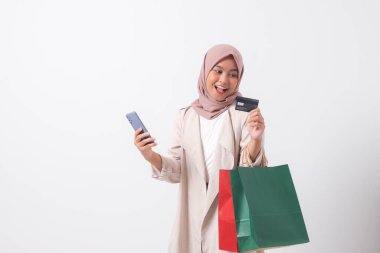 Alışveriş torbaları ve kredi kartı taşıyan, rahat giyimli, cep telefonu kullanan heyecanlı Asyalı kadının portresi. Alışverişkolik kız ve indirim satın alma konsepti. Beyaz arkaplanda izole edilmiş resim