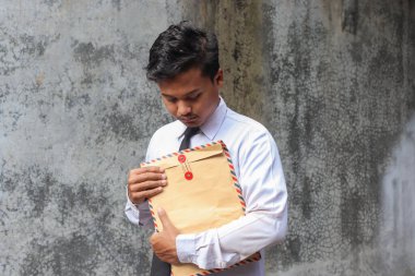 Beyaz gömlekli, içinde özgeçmişi olan kahverengi bir zarf taşıyan işsiz Asyalı bir adamın portresi. Personel alımı konsepti.