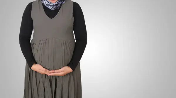 Karnının üstünde elleri olan tanınmayan hamile bir müslüman kadının portresi. Beyaz arkaplanda izole edilmiş resim
