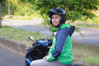 Back view of online taxi rider wearing green jacket and helmet, riding motorcycle while on the way to pick up customer. Transportation application concept. clipart