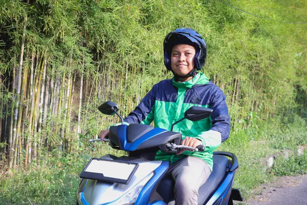 Çevrimiçi taksi şoförü yeşil ceket ve kask giyiyor, müşteri almaya giderken motosiklet sürüyor. Ulaşım uygulaması kavramı.