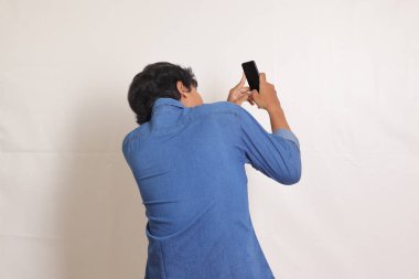 Elinde cep telefonu olan mavi gömlekli heyecanlı Asyalı adamın arka plan portresi. Reklam konsepti. Beyaz arkaplanda izole edilmiş resim