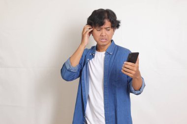 Mavi gömlekli mutsuz Asyalı adamın portresi cep telefonu tutarken kızgın el hareketi yaparken hayal kırıklığına uğradı. Beyaz arkaplanda izole edilmiş resim