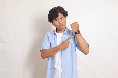 Mavi gömlekli heyecanlı Asyalı adamın portresi kol saatine bakıyor. Reklam konsepti. Beyaz arkaplanda izole edilmiş resim