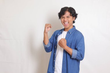 Mavi gömlekli çekici Asyalı adamın portresi yumruğunu kaldırarak başarıyı kutluyor. Beyaz arkaplanda izole edilmiş resim