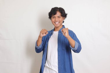 Mavi gömlekli çekici Asyalı adamın portresi yumruğunu kaldırarak başarıyı kutluyor. Beyaz arkaplanda izole edilmiş resim