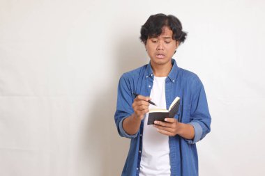 Fikir hakkında düşünürken mavi gömlekli kafası karışmış Asyalı adamın portresi. Beyaz arkaplanda izole resimler