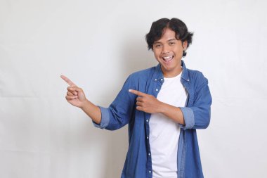 Mavi tişörtlü çekici Asyalı adamın portresi. Ürünleri sunuyor, yan tarafı işaret ediyor. Reklam ve pazarlama konsepti. Beyaz arkaplanda izole resimler