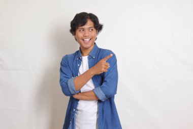 Mavi tişörtlü mutlu Asyalı bir adamın portresi. Ürünü sunuyor, yan tarafı işaret ediyor. Reklam ve pazarlama konsepti. Beyaz arkaplanda izole resimler