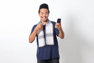 Heyecanlı Asyalı Müslüman adamın cep telefonu tutan ve malı parmağıyla gösteren sargılı eşarp taktığı portresi. Sosyal medya konsepti. Beyaz arkaplanda izole edilmiş resim