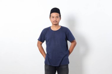 Beyaz arka planda duran kafatası şapkalı Asyalı Müslüman adamın hazırlıksız portresi.