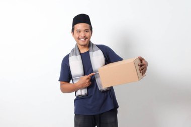 Heyecanlı Asyalı Müslüman adamın portresi sargılı atkı ve karton kutu taşıyan kafatası şapkası. Beyaz arkaplanda izole