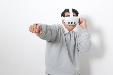 Sanal gerçeklik VR cihazı kullanan Asyalı bir adamın portresi, oyunda düşmanını yumruklamaya ve onunla savaşmaya çalışıyor. Beyaz arkaplanda izole edilmiş resim