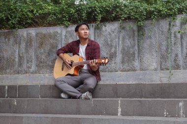 Sabahleyin şehir parkında gitar çalan Asyalı çekici bir adamın açık hava çekimi.