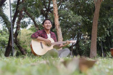 Sabahleyin şehir parkında gitar çalan Asyalı çekici bir adamın açık hava çekimi.