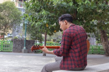 Sabahleyin şehir parkında gitar çalan Asyalı çekici bir adamın açık hava çekimi.
