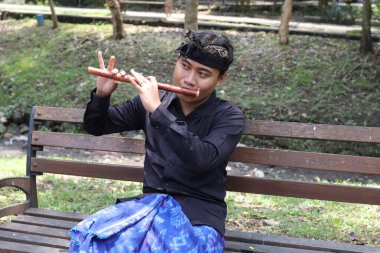 Portrait of Balinese man playing traditional bamboo flute at park in the morning clipart