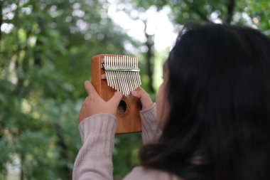 Portrait of Asian woman in sweater playing kalimba music box at city park clipart