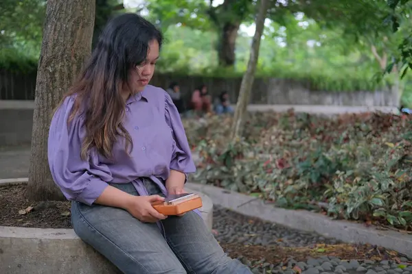 Asyalı kadın güneşli bir yaz gününde şehir parkında geleneksel kalimba çalıyor. Yeşilliklerle çevrili, huzurlu bir anın tadını çıkarıyor, müziği doğanın sükunetiyle harmanlıyor.