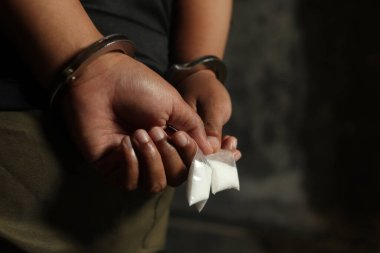 Uyuşturucu satıcısı elleri kelepçeli, elinde uyuşturucu paketiyle tutuklandı. Tehlike ve uyuşturucu tehdidi kavramı. Dramatik ışık portresi
