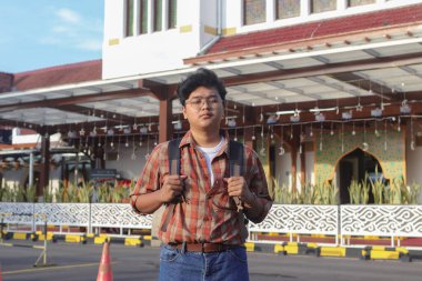 Sırt çantası taşıyan Asyalı bir adamın portresi tren istasyonunun önünde duruyordu.