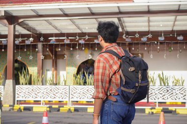 Sırt çantası taşıyan Asyalı bir adamın arka plan portresi tren istasyonunun önünde duruyordu.