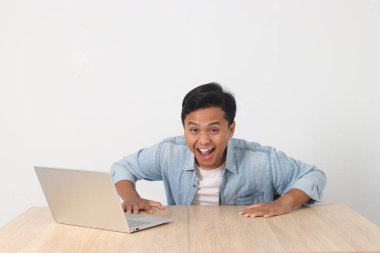 Kendine güvenen Asyalı adam, gülümsüyor ve dizüstü bilgisayarıyla çalışıyor, görevinin keyfini çıkarıyor, beyaz arka planda izole edilmiş.