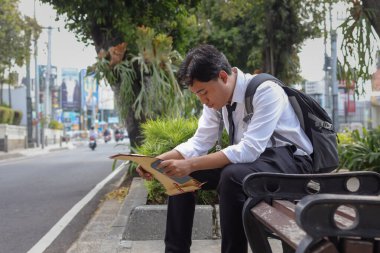 Beyaz gömlekli Asyalı iş arayanın portresi. Özgeçmişini içeren kahverengi bir zarf tutarken iş arıyor. Bankta oturuyor. Personel alımı konsepti