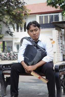 Beyaz gömlekli Asyalı iş arayanın portresi. Özgeçmişini içeren kahverengi bir zarf tutarken iş arıyor. Bankta oturuyor. Personel alımı konsepti