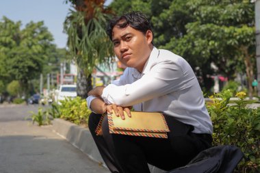 Takım elbiseli Asyalı bir çalışanın portresi. Elinde özgeçmişi olan kahverengi bir zarf var. Kaldırımda elleri başının üstünde oturuyor. İşten çıkarma ve işsizlik kavramı