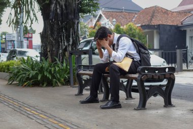 Özgeçmişini içeren kahverengi bir zarf tutarken iş arayan Asyalı bir çalışanın portresi, elleri başının üstünde bankta oturuyor. İş arayan işe alım kavramı