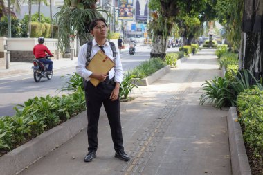 Beyaz gömlekli Asyalı bir iş arayanın portresi. İçinde özgeçmişi olan kahverengi bir zarfı şehir caddesinde dururken iş arıyor. Personel alımı konsepti