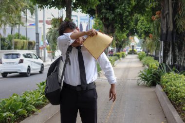 Özgeçmişini içeren kahverengi bir zarf taşırken terini silen takım elbiseli Asyalı bir iş arayanın portresi. Personel alımı konsepti.