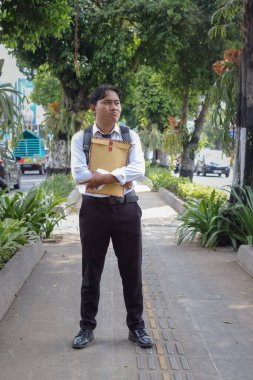 Beyaz gömlekli Asyalı bir iş arayanın portresi. İçinde özgeçmişi olan kahverengi bir zarfı şehir caddesinde dururken iş arıyor. Personel alımı konsepti