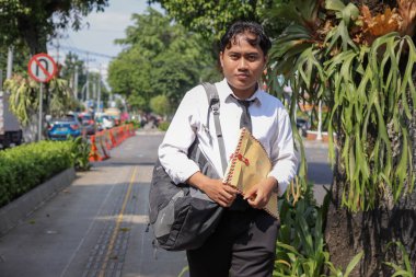 Beyaz gömlekli Asyalı bir iş arayanın portresi. İçinde özgeçmişi olan kahverengi bir zarfı tutarken iş arıyor. Şehir caddesinde aceleyle yürüyor. Personel alımı konsepti