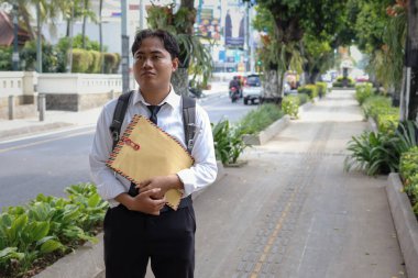 Beyaz gömlekli Asyalı bir iş arayanın portresi. İçinde özgeçmişi olan kahverengi bir zarfı şehir caddesinde dururken iş arıyor. Personel alımı konsepti