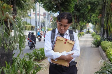 Beyaz gömlekli Asyalı bir iş arayanın portresi. İçinde özgeçmişi olan kahverengi bir zarfı tutarken iş arıyor. Şehir caddesinde aceleyle yürüyor. Personel alımı konsepti