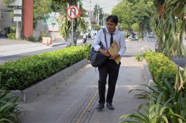 Beyaz gömlekli Asyalı bir iş arayanın portresi. İçinde özgeçmişi olan kahverengi bir zarfı tutarken iş arıyor. Şehir caddesinde aceleyle yürüyor. Personel alımı konsepti